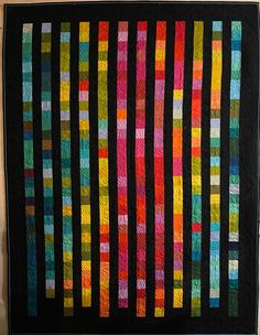 a black quilt with multicolored strips on the front and back, hanging from a wall