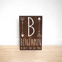 a wooden block with the name benjamin on it and arrows in white ink