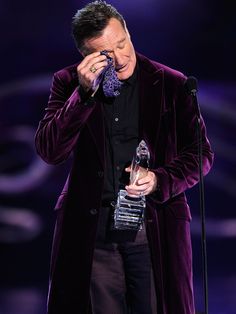 a man in a purple suit holding an award up to his face while standing next to a microphone