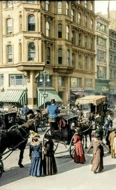 an old time photo of people and horses on the street in front of tall buildings