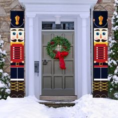 a door with a wreath and nutcrackers on it in front of snow covered trees