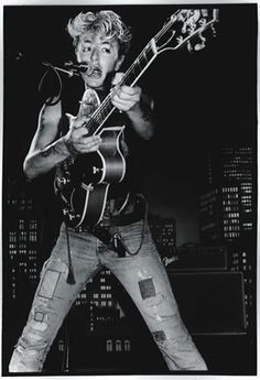 a black and white photo of a man holding a guitar in front of a cityscape