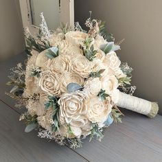 a bridal bouquet with white flowers and greenery sits on a table next to a mirror