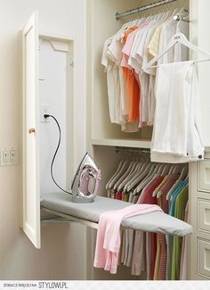 an ironing board and clothes hanging on a rail in a closet with white drawers