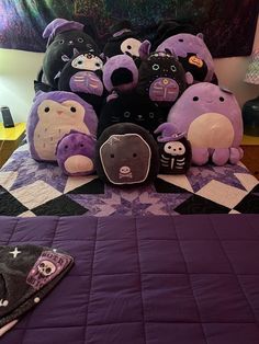 there are many stuffed animals on the bed with purple sheets and black pillow cases in front of them