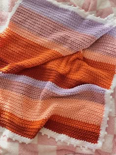 an orange, pink and purple striped blanket laying on top of a white table cloth