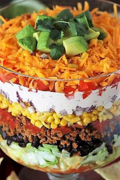 a layered salad in a glass dish with cheese, tomatoes, corn and avocado