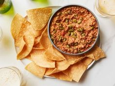 a white plate topped with chips and salsa next to two glasses filled with beers