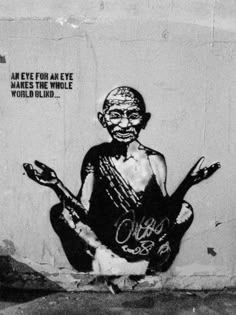 a black and white photo of a person sitting in front of a wall with graffiti on it