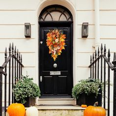 two pumpkins sitting in front of a black door with a wreath on the top