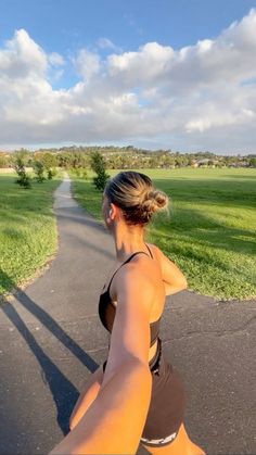 a woman is running down the road with her shadow on the ground and grass in the background