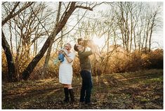 a man and woman are standing in the woods with their baby girl, who is wearing a white dress