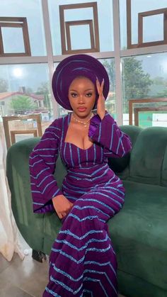 a woman in a purple dress and hat sitting on a green couch with her hand up to her face