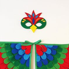 a mask and some paper decorations on a white wall with a green ribbon around it