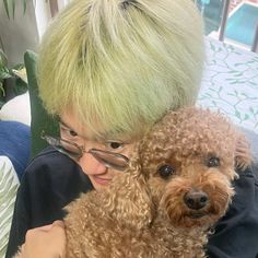 a woman with green hair and glasses holding a brown poodle dog in her lap