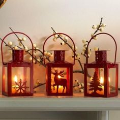 three red lanterns with candles in them on a mantle next to christmas trees and snowflakes