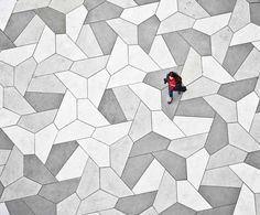 an aerial view of a person sitting on the ground in front of a pattern of grey and white tiles