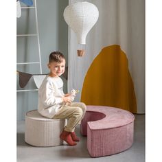 a young boy sitting on top of a stool next to a pink ottoman and lamp