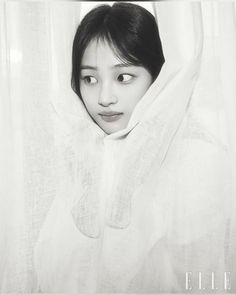 black and white photograph of a young woman peeking out from behind a sheered curtain