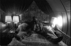 a man laying on top of a bed next to two lamps in a room filled with curtains