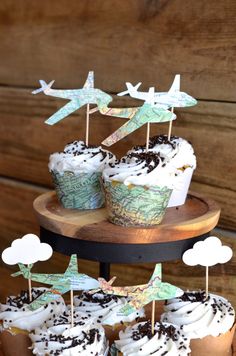 cupcakes with white frosting and airplanes on top are sitting on a wooden tray