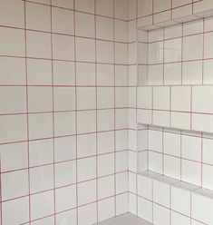 a bathroom with red and white tiles on the walls, shelves in the shower stall