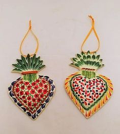 two ceramic fruit ornaments hanging from strings on a white wall, one has a heart and the other is a strawberry