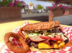 a large hamburger and onion rings on a table with some flowers in the back ground