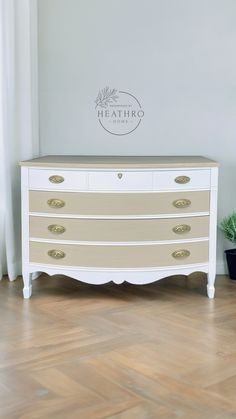 a white dresser sitting on top of a hard wood floor next to a potted plant