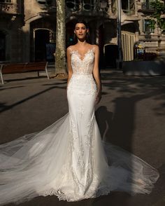 a woman in a white wedding dress standing on the street with her hands behind her back