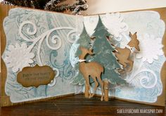 an open card with two deer and a christmas tree on the inside, in front of a pine tree