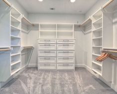 an empty walk in closet with white shelves and drawers