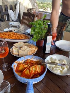 a wooden table topped with plates and bowls of food next to wine glasses on top of it