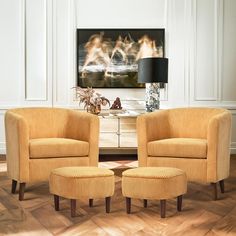 two chairs and a footstool in front of a fireplace with a painting on the wall