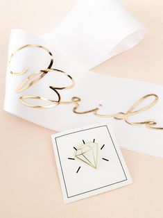 a piece of white paper with gold lettering on it next to a pair of scissors