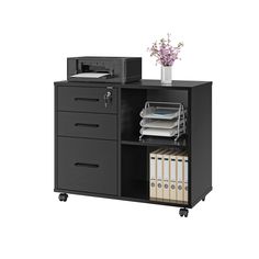 a black filing cabinet with drawers and file folders on wheels next to a printer