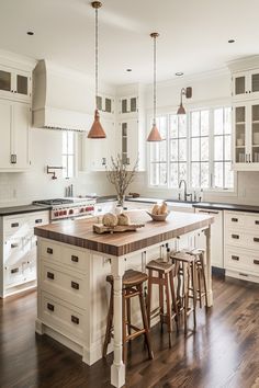 a large kitchen with white cabinets and wooden flooring is pictured in this image, there are three stools at the center of the island