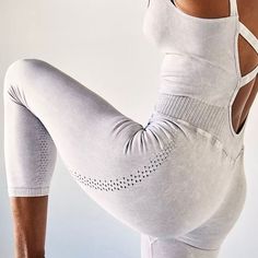 a woman in white sports bra and leggings stretching her back with one hand