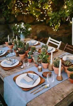 the table is set with plates, silverware and succulents in pots