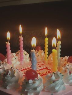 a birthday cake with lit candles on it and frosted cupcakes in the middle