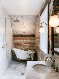 a bathtub and sink in a bathroom with exposed brick walls, white marble counter tops and gold fixtures