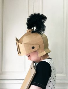 a young child wearing a cardboard helmet with feathers on it's head and carrying a book