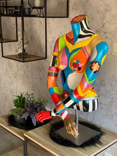 a colorful mannequin sitting on top of a table next to a potted plant