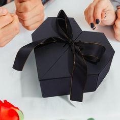 a woman is opening a black gift box with a ribbon on the top and two hands holding it