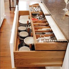 an open drawer in a kitchen filled with dishes and utensils on the counter