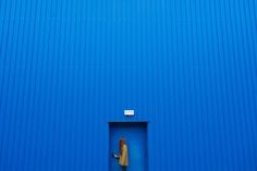 a person standing in a blue door with their hand on his hip and looking at the ground