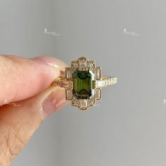 a woman's hand holding an engagement ring with a green tourmaline surrounded by diamonds