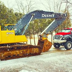 two large trucks are parked next to each other on the snow covered road in front of some trees