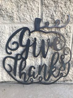 a metal sign that says give thanks on the side of a building with an apple