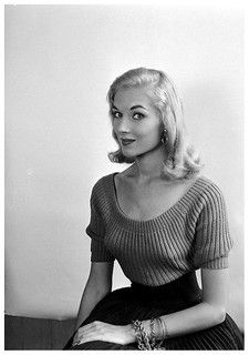 a black and white photo of a woman sitting on a table with her hands in her pockets